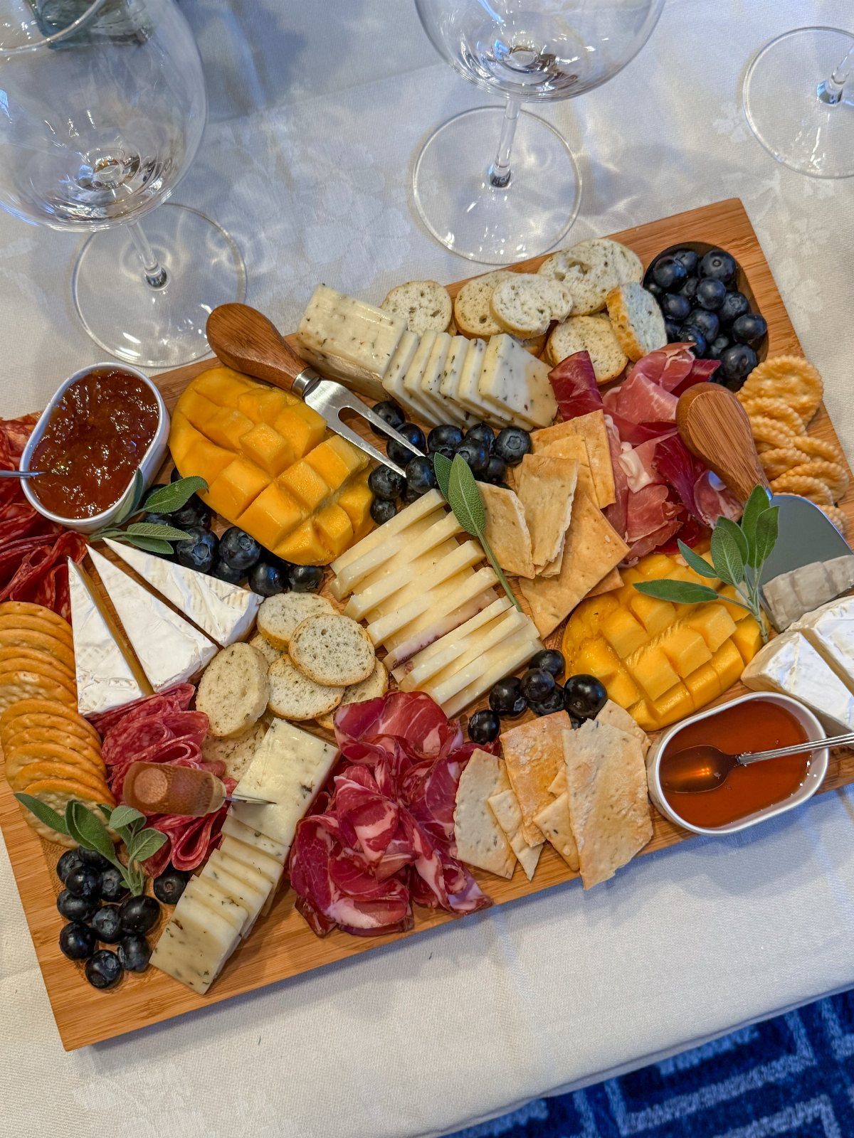Charcuterie board with assorted cheeses, meats, blueberries, and crackers on a white tablecloth.
