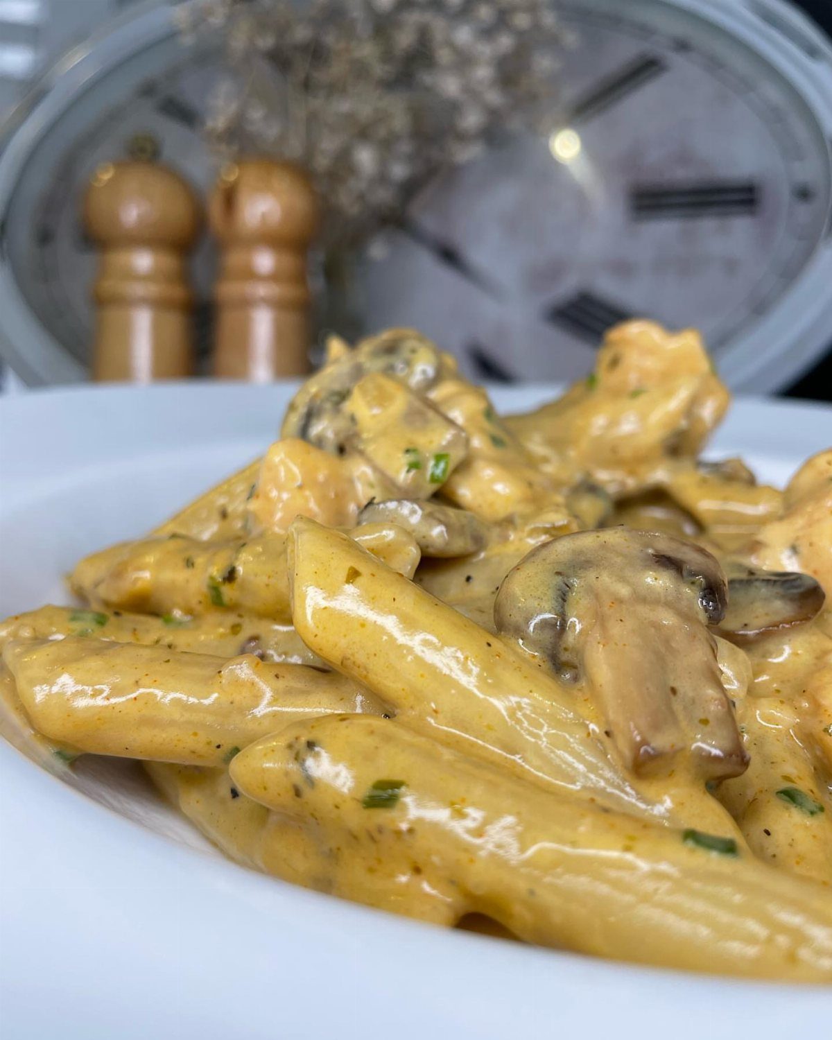 Penne pasta in a creamy sauce with sliced mushrooms and fresh green herbs.