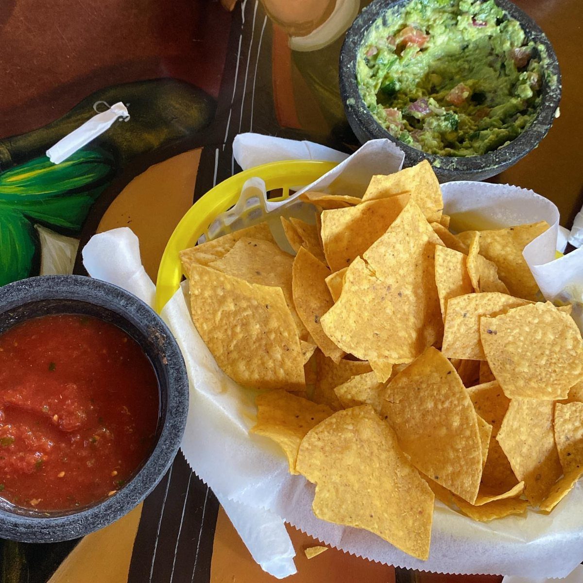Tortilla chips in a basket with bowls of red salsa and green guacamole.