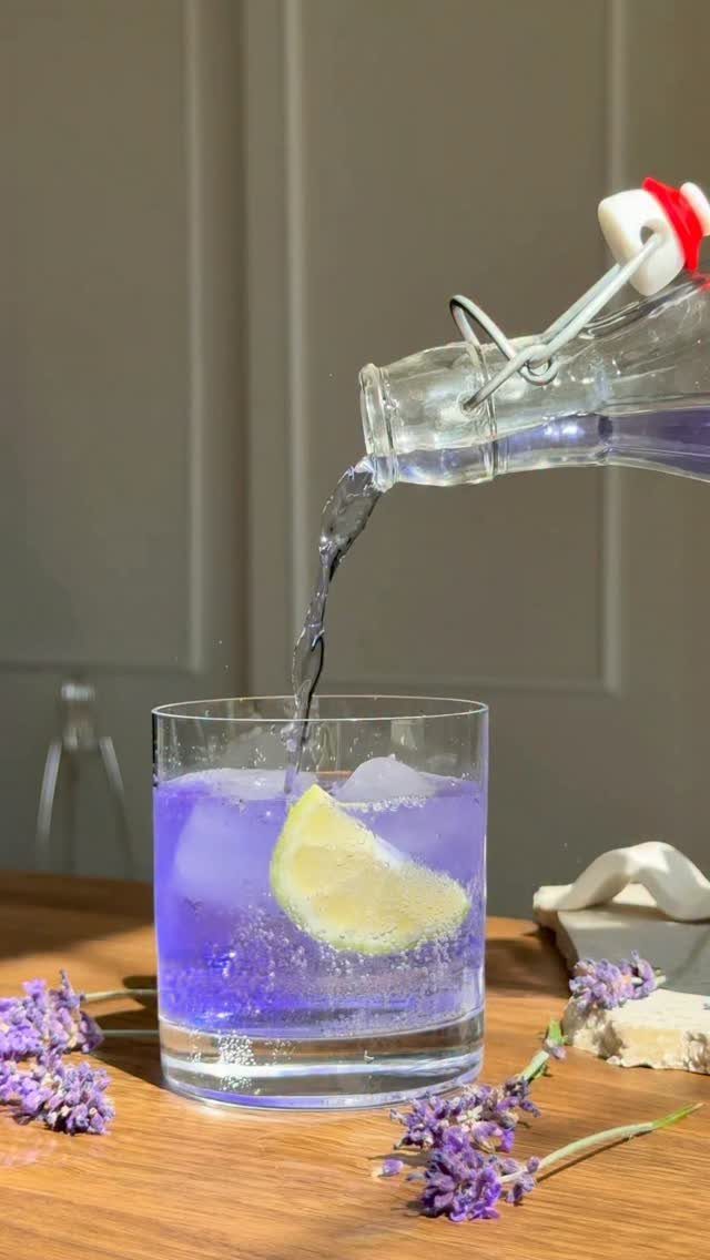 Purple lavender lemonade being poured into a glass with ice and lemon.