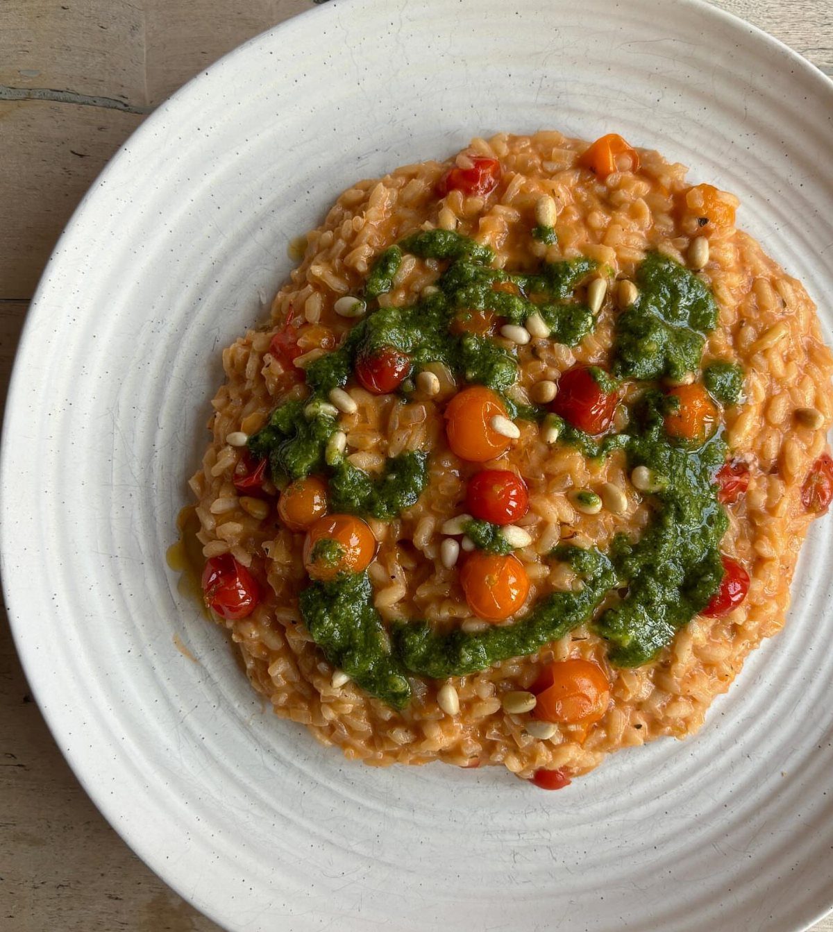 Creamy orange risotto topped with green pesto, cherry tomatoes, and pine nuts.