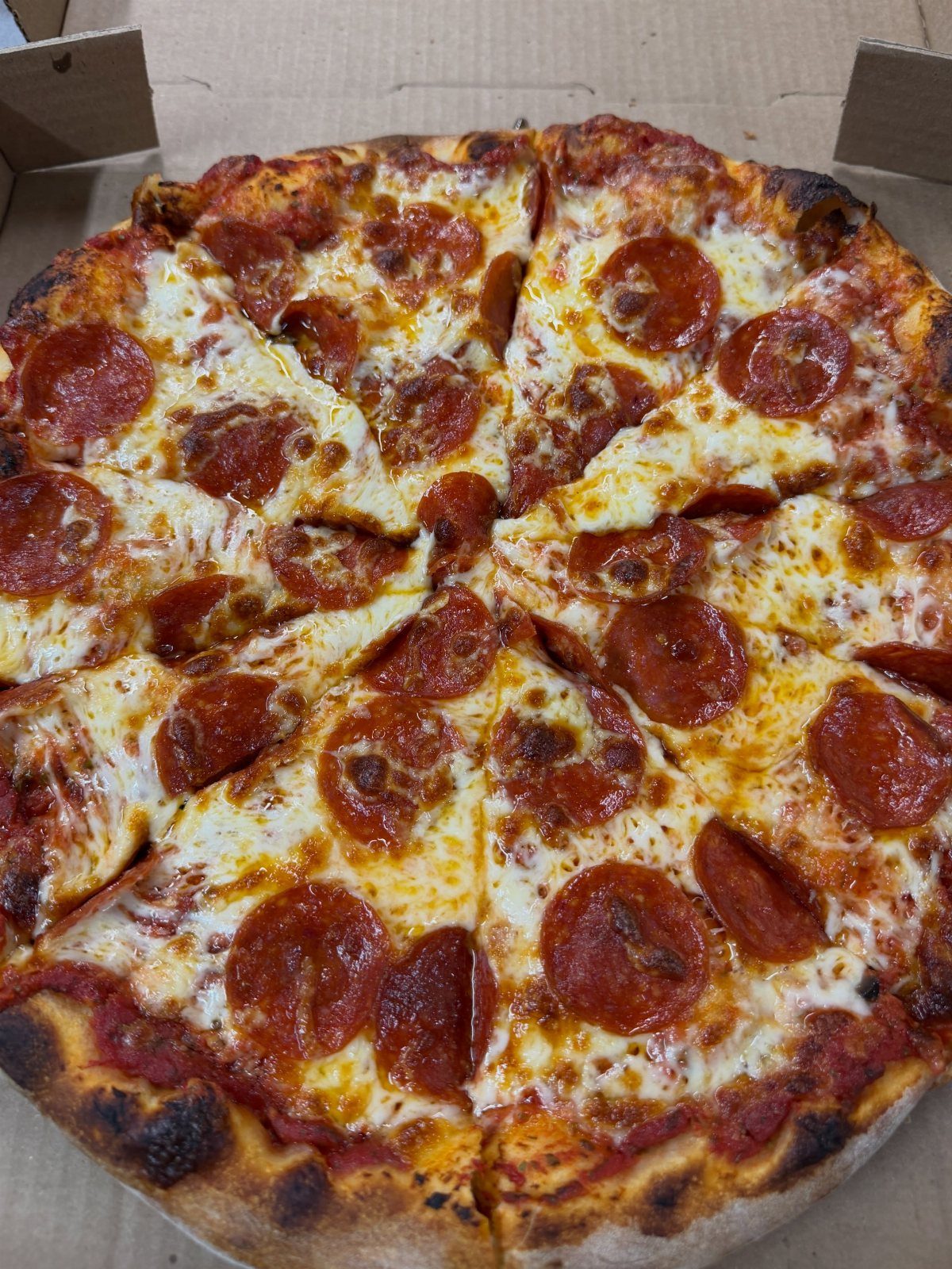 Pepperoni pizza with melted cheese inside a brown cardboard delivery box.