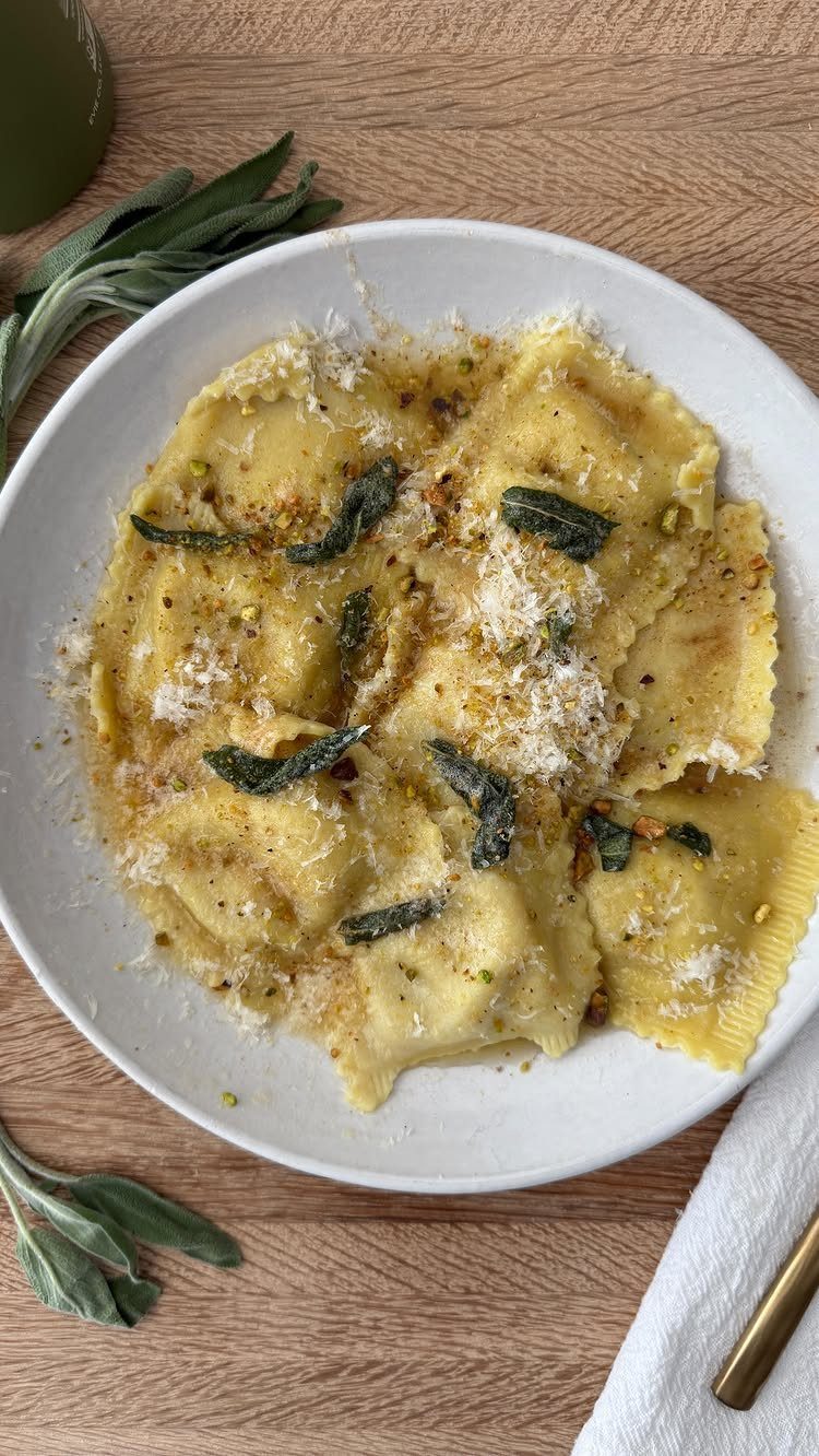 Ravioli with sage butter sauce and parmesan cheese on a white plate.