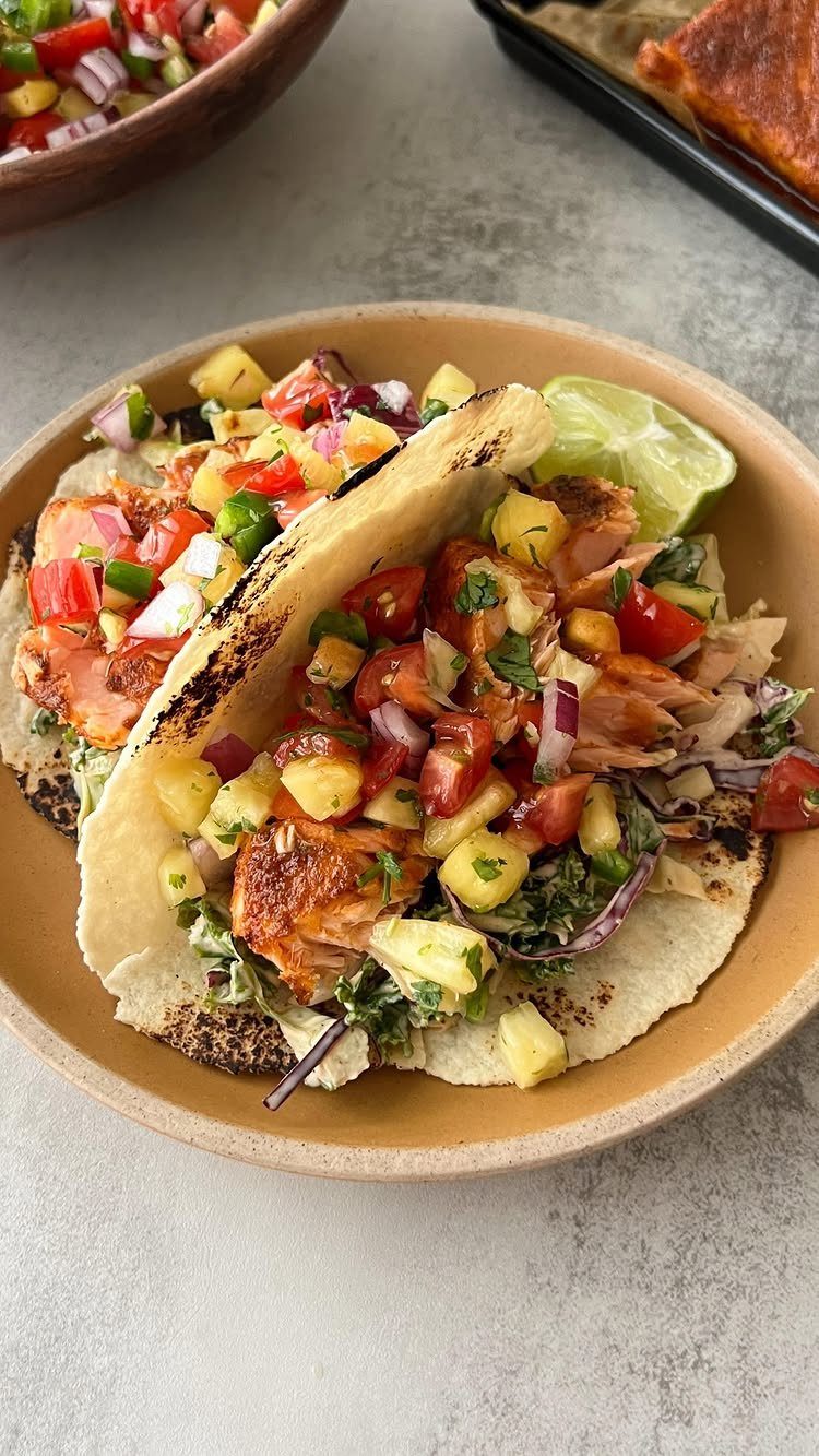 Salmon tacos topped with pineapple salsa and a lime wedge on a plate
