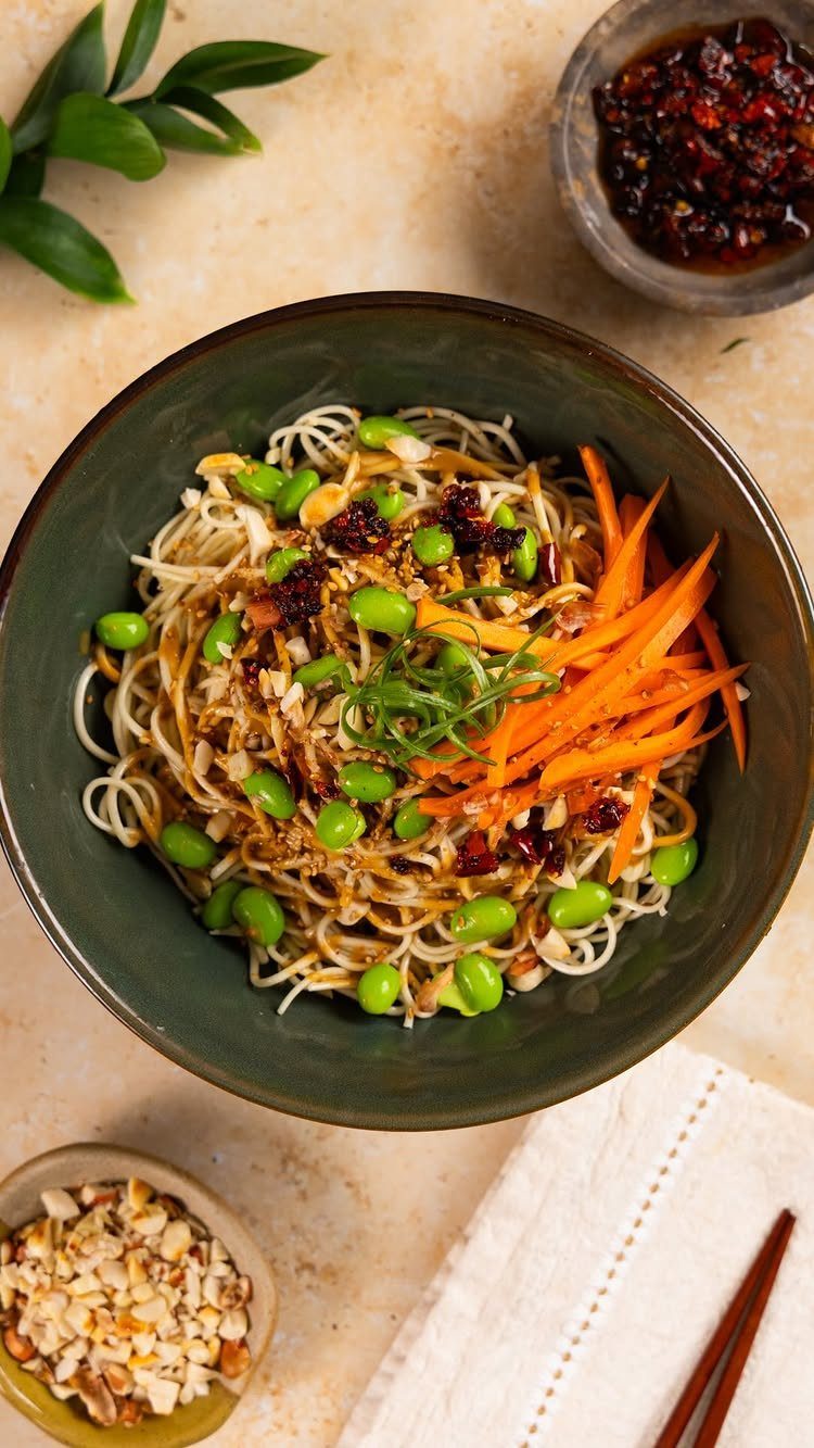 Cold sesame noodles in a green bowl with edamame and shredded carrots.