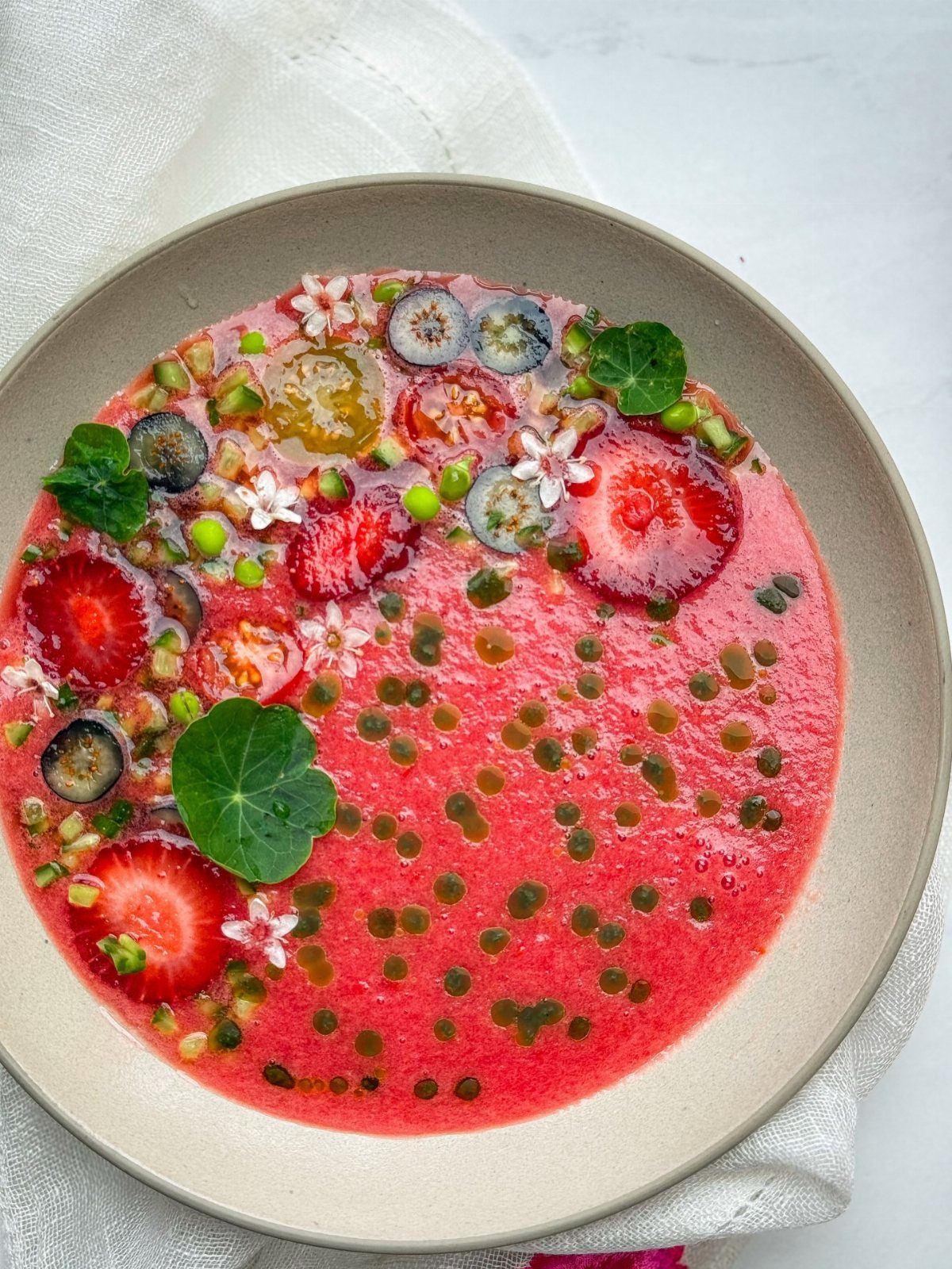 Pink chilled gazpacho soup topped with fresh strawberries, blueberries, and green herbs.