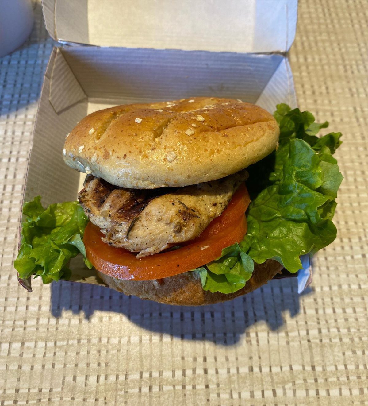 Grilled chicken sandwich with tomato and lettuce on a sesame bun in takeout box