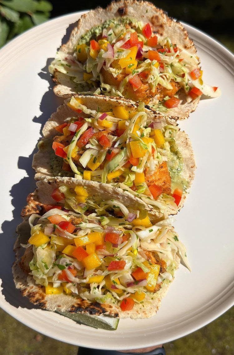 Three fish tacos with colorful vegetable slaw on a white ceramic plate.