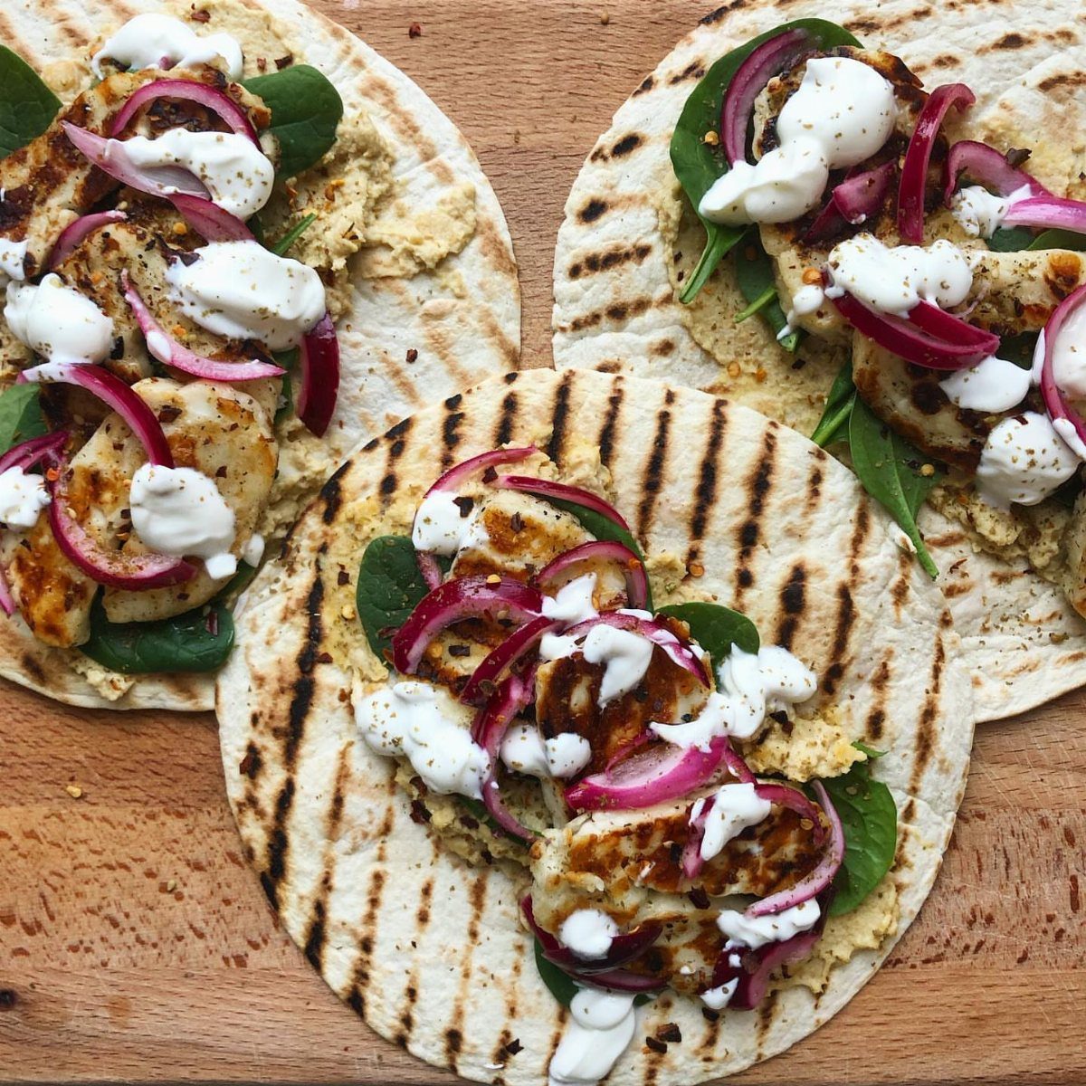 Grilled chicken and hummus wraps with red onion and white sauce on flatbread