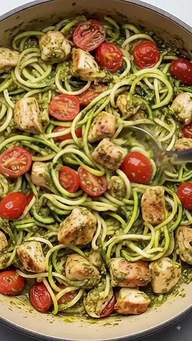 Zucchini noodles with pesto, chicken chunks, and cherry tomatoes in a cooking pan.