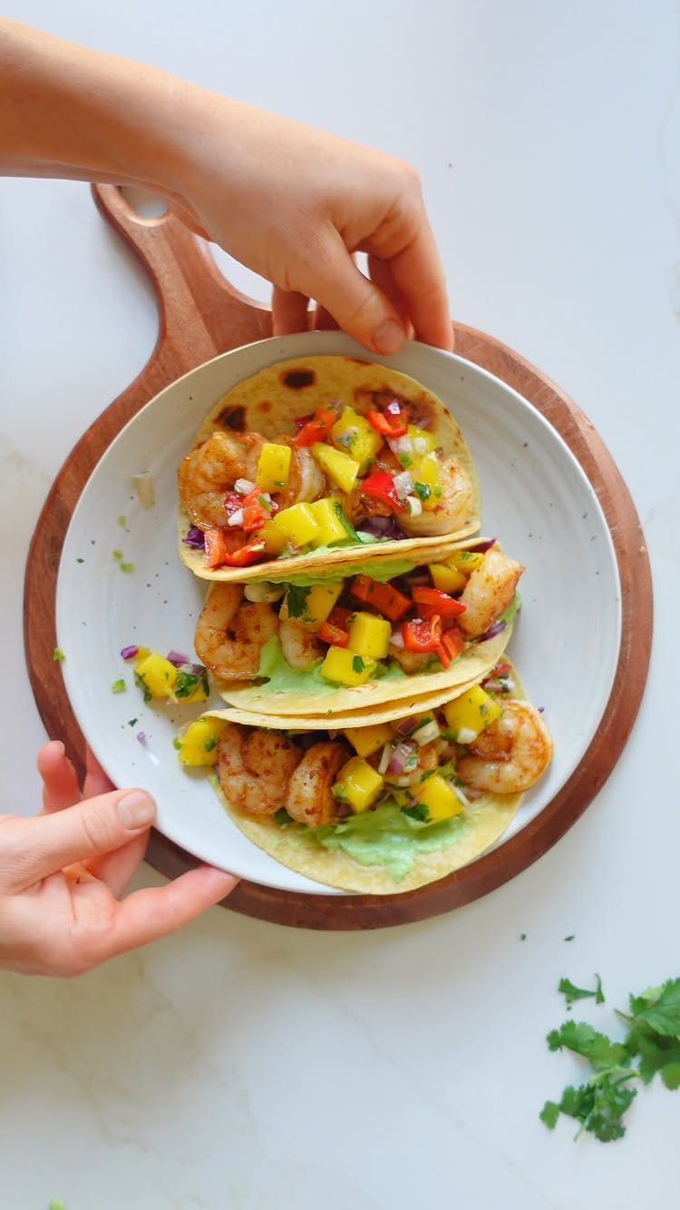 Shrimp tacos with mango salsa and green sauce on a white plate.