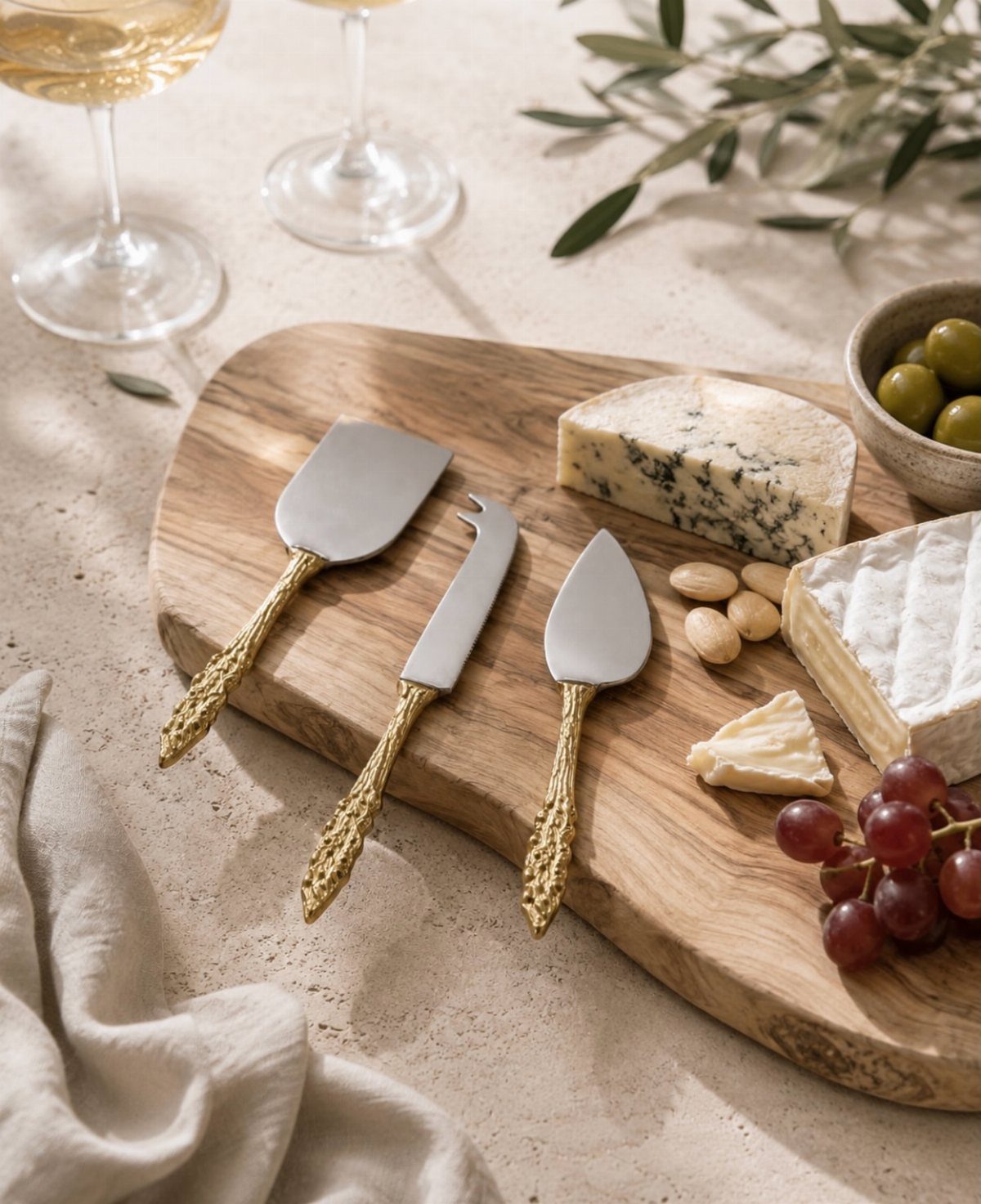 Organic wooden serving board with various cheeses, grapes, nuts, and gold cheese knives.
