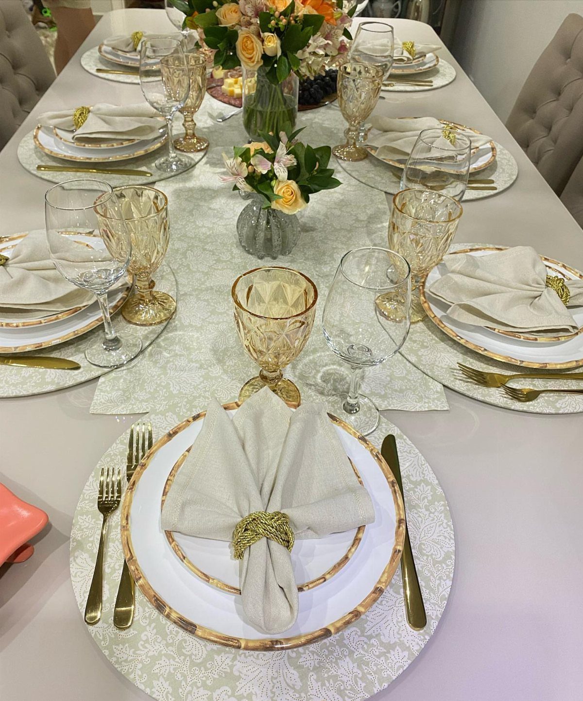 Formal dining table setting with gold-rimmed plates, gold cutlery, and floral centerpieces.