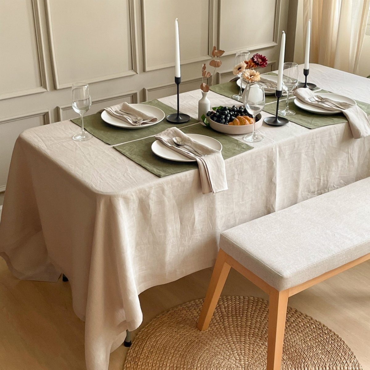 Dining table with beige tablecloth and green placemats set with white plates and candles