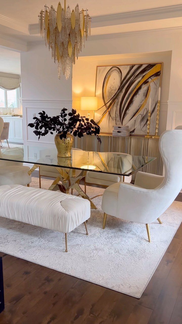 Glass dining table with gold legs, white chairs, and a gold floral centerpiece.