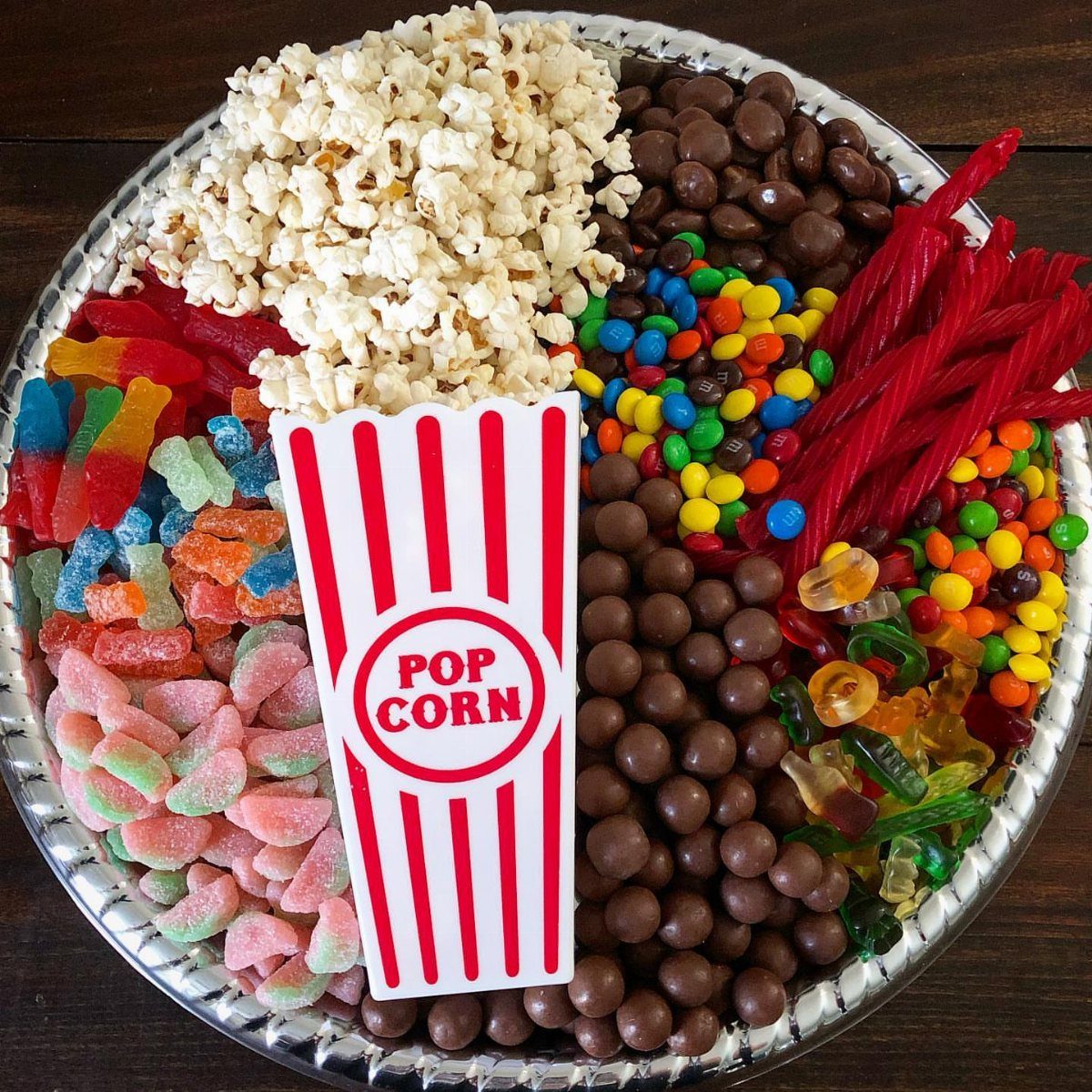 Assorted movie snacks including popcorn, chocolate, and colorful candies on a silver tray.