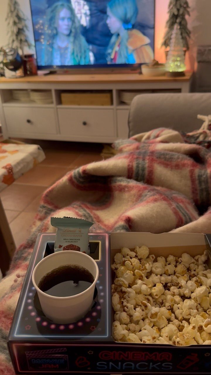 Cinema snack box with popcorn and a drink on a cozy plaid blanket.