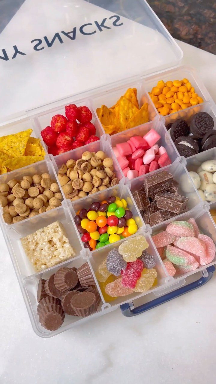 Clear plastic snack box filled with assorted candies, chocolates, and savory snacks.