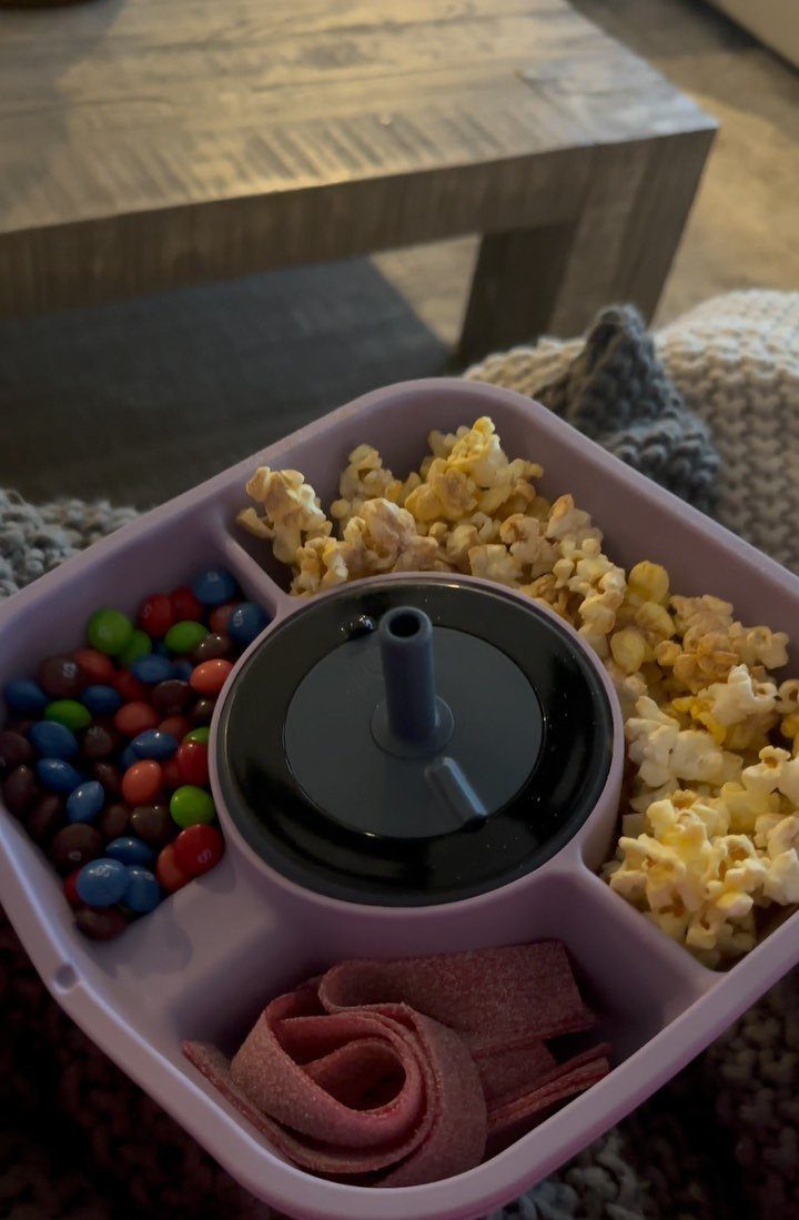 Purple divided snack tray with popcorn, colorful candies, and fruit leather strips.