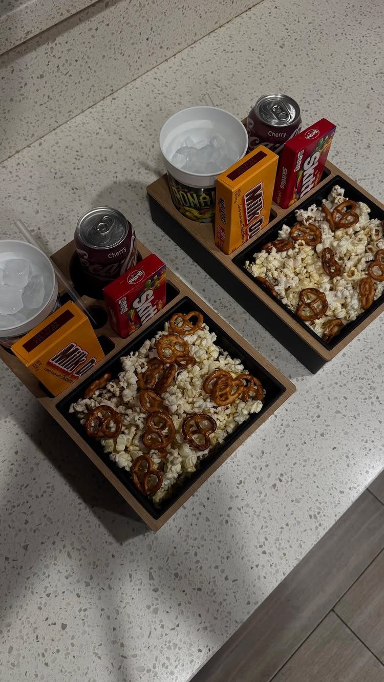 Two wooden snack boxes filled with popcorn, pretzels, candy, and soda cans.