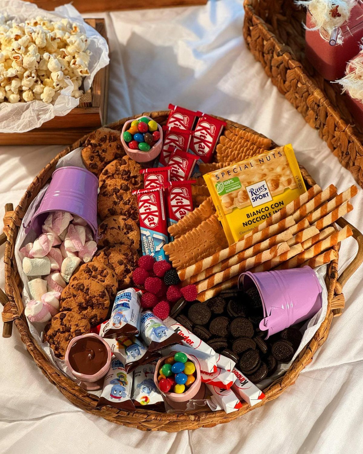 Wicker basket filled with cookies, marshmallows, raspberries, and assorted packaged movie snacks.