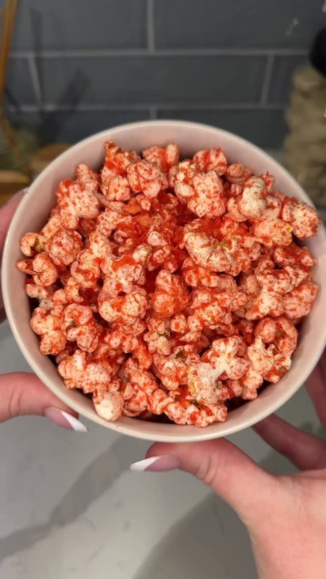 Orange-red seasoned popcorn in a white bowl held by two hands.