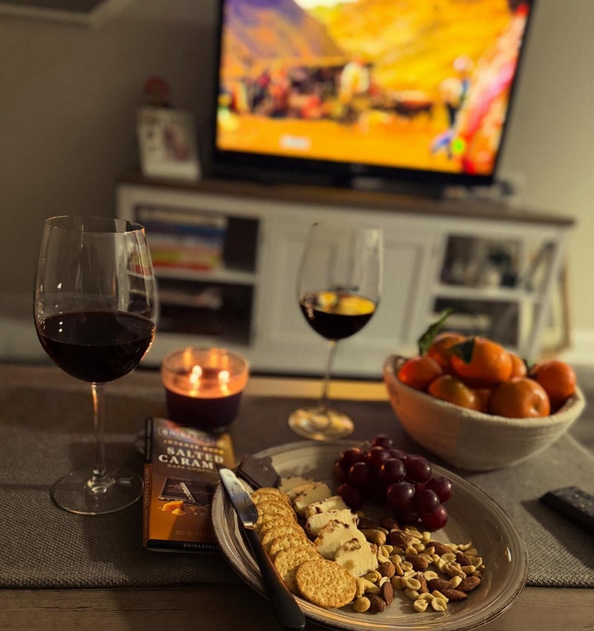 Plate of cheese, crackers, grapes, and nuts with red wine and tangerines.