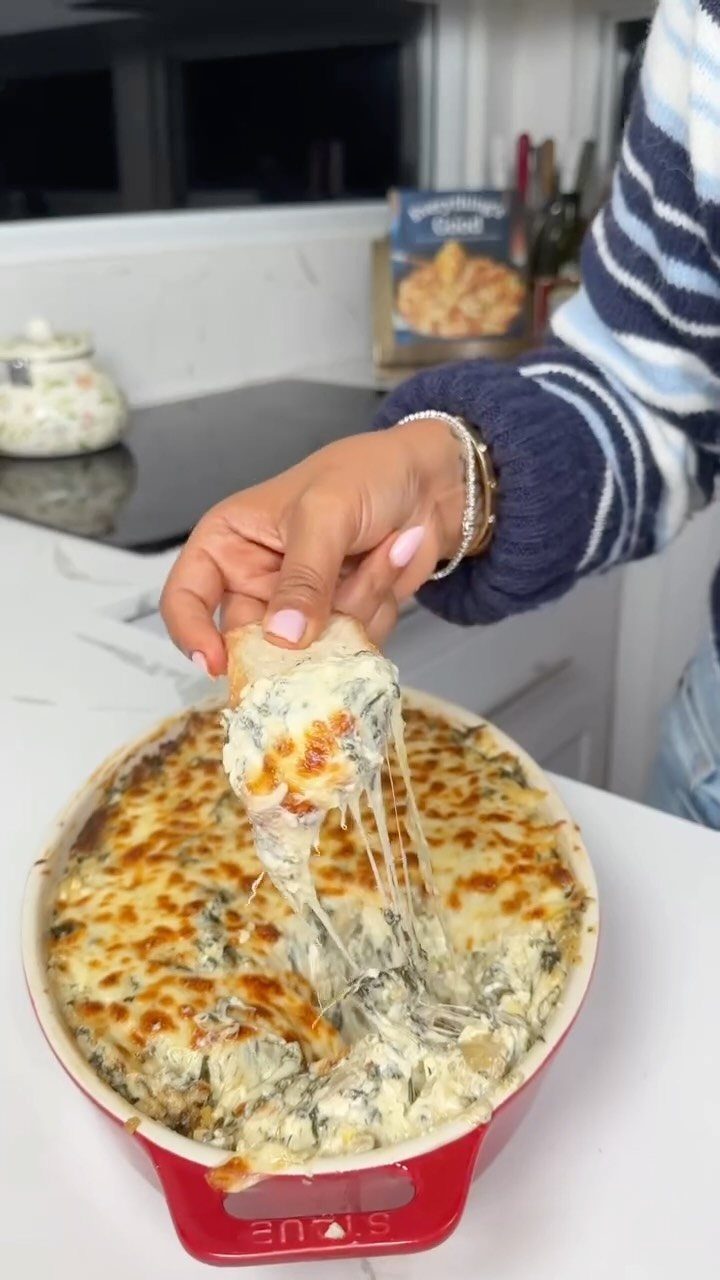 Cheesy spinach artichoke dip in a red dish with a bread scoop