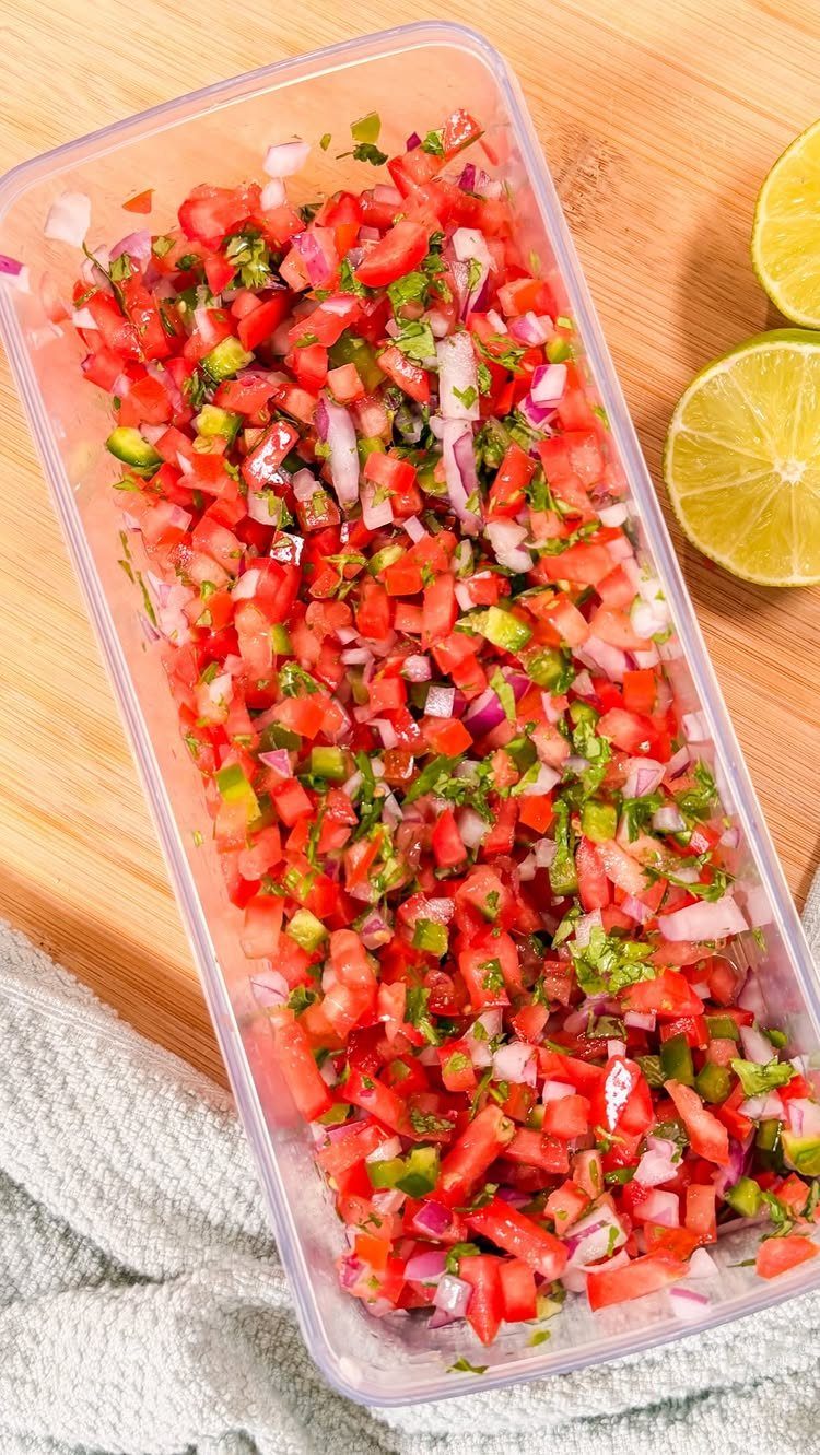 Fresh pico de gallo salsa in a plastic container with lime halves nearby.