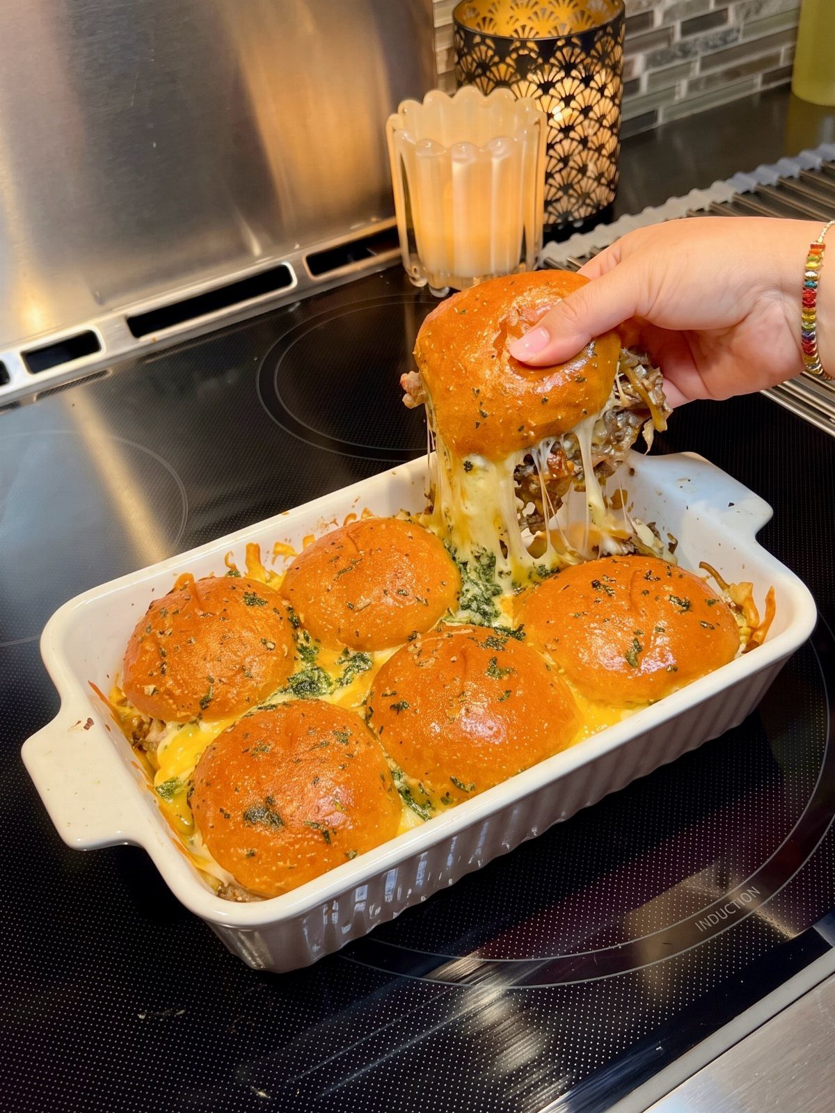 Mini burger sliders with melted cheese being lifted from a white baking dish.