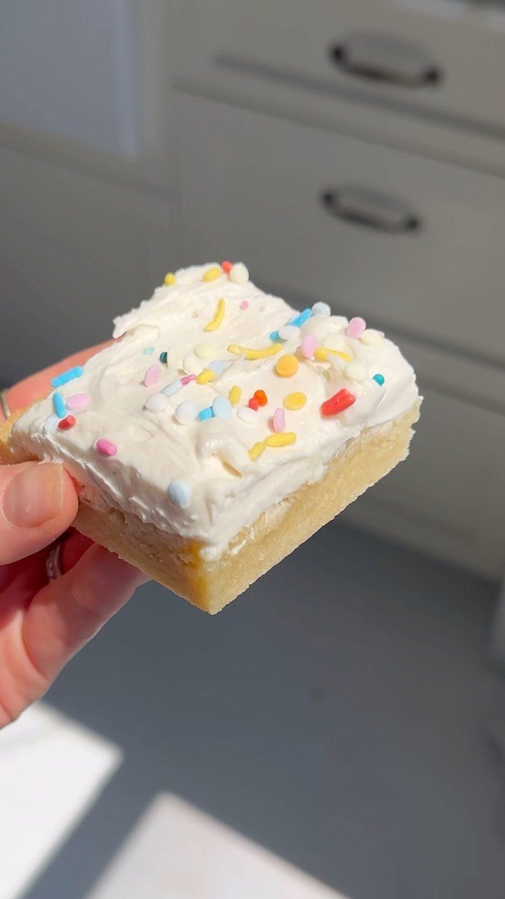 Sugar cookie bar with white frosting and rainbow sprinkles held in a hand.