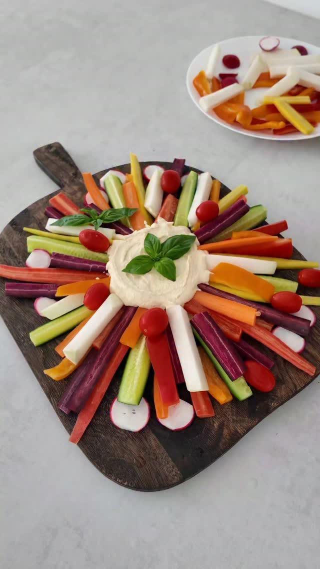 Vegetable sticks arranged radially around a bowl of hummus on a wooden board.