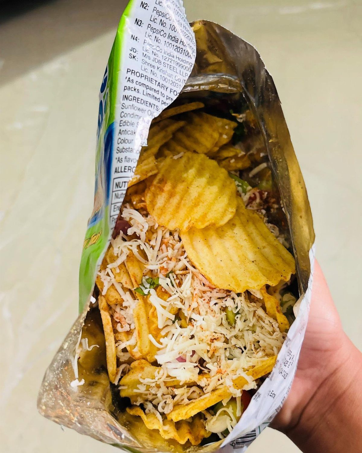 Ridged potato chips topped with shredded cheese and vegetables inside a chip bag.