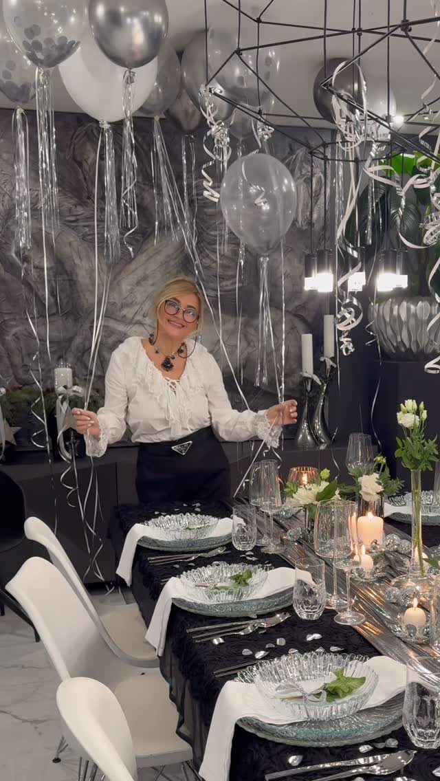 Woman standing behind a festive New Year's Eve table with silver and black decorations.