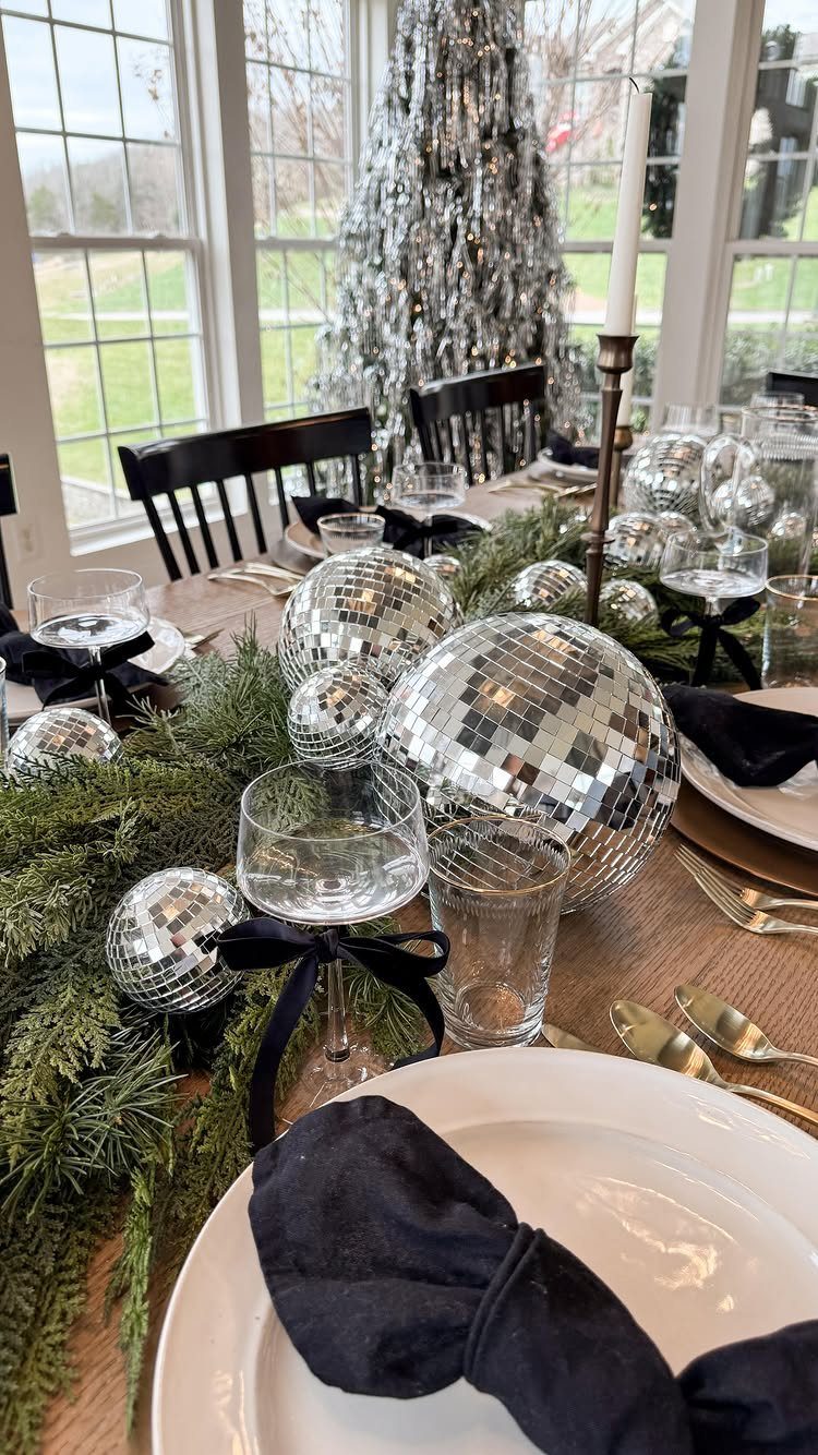 Dining table decorated with silver disco balls, pine greenery, and black napkins.
