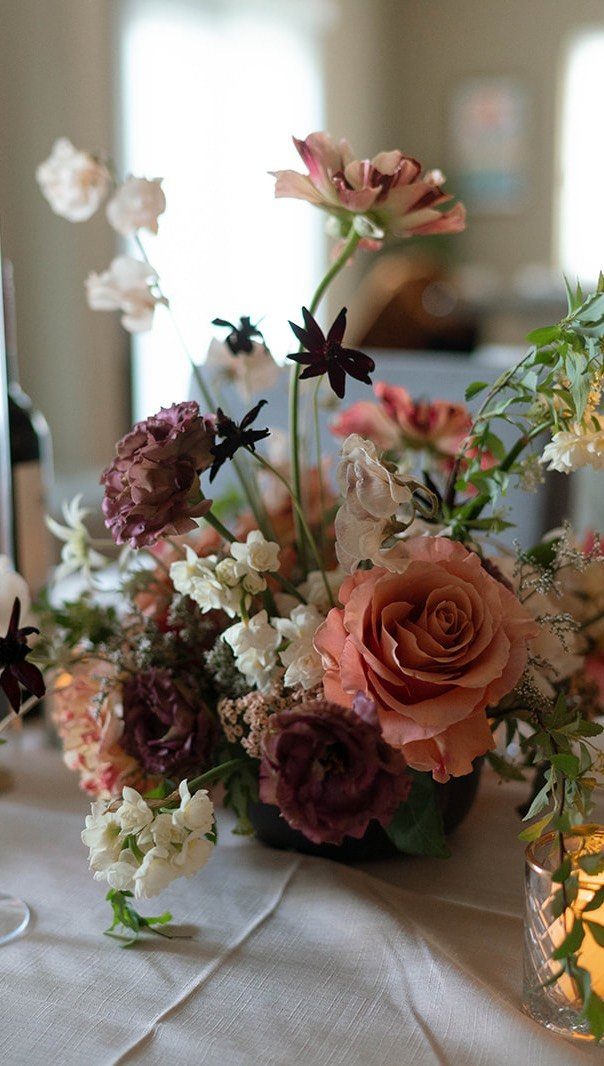 Floral centerpiece with peach and burgundy roses on a white linen table.