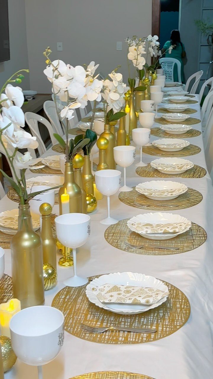 Elegant table setting with gold placemats, white orchids in gold bottles, and white dinnerware.