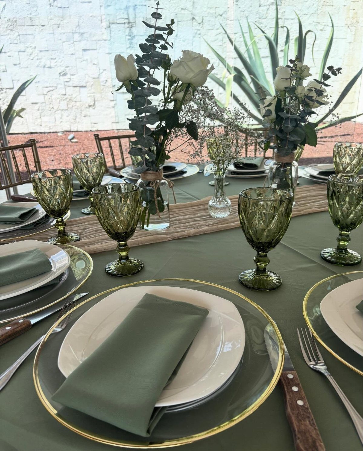 Formal table setting with green linens, gold-rimmed plates, and eucalyptus greenery centerpieces.