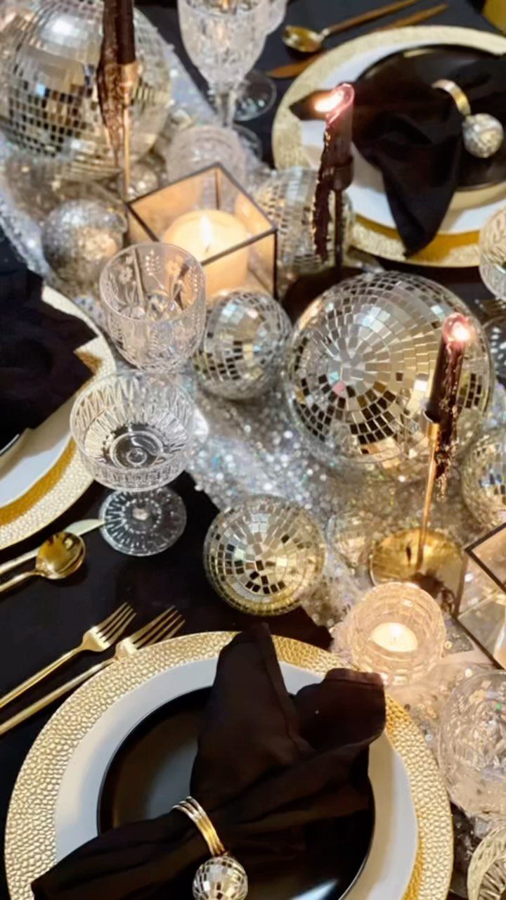 Festive table setting with silver disco balls, gold cutlery, and black plates.
