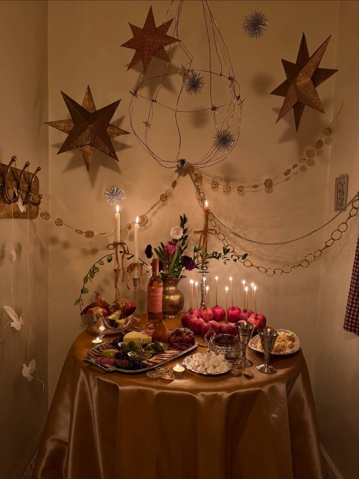 Gold table setting with lit white taper candles, fruit, and star wall decorations.