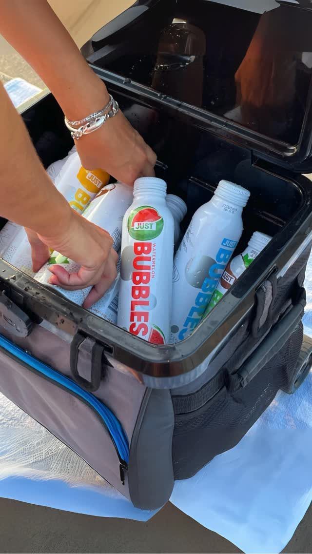 Hands reaching for sparkling water bottles inside a grey and blue portable cooler.