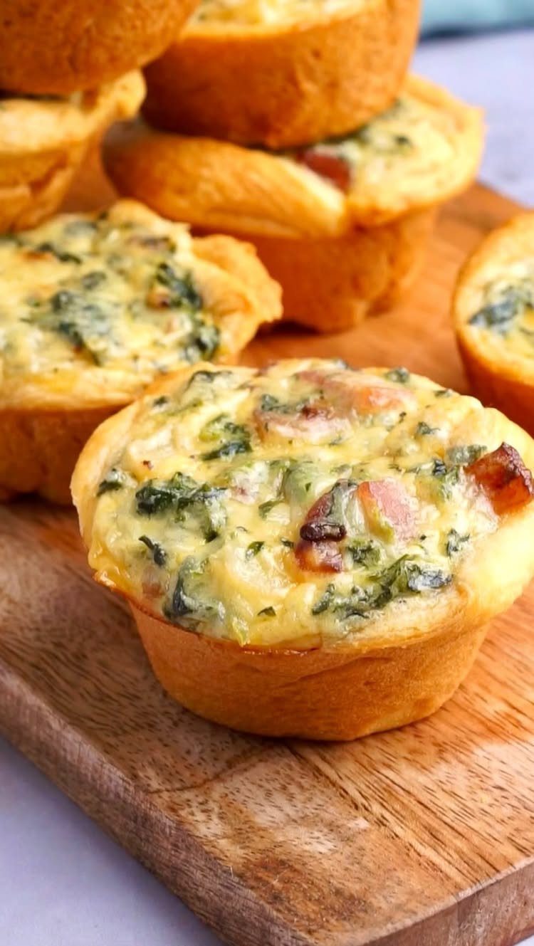 Mini quiches with spinach and bacon on a wooden serving board.