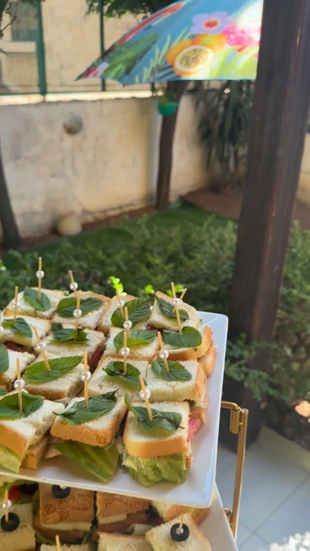 Mini sandwiches with mint leaves and pearl toothpicks on a white tiered platter.