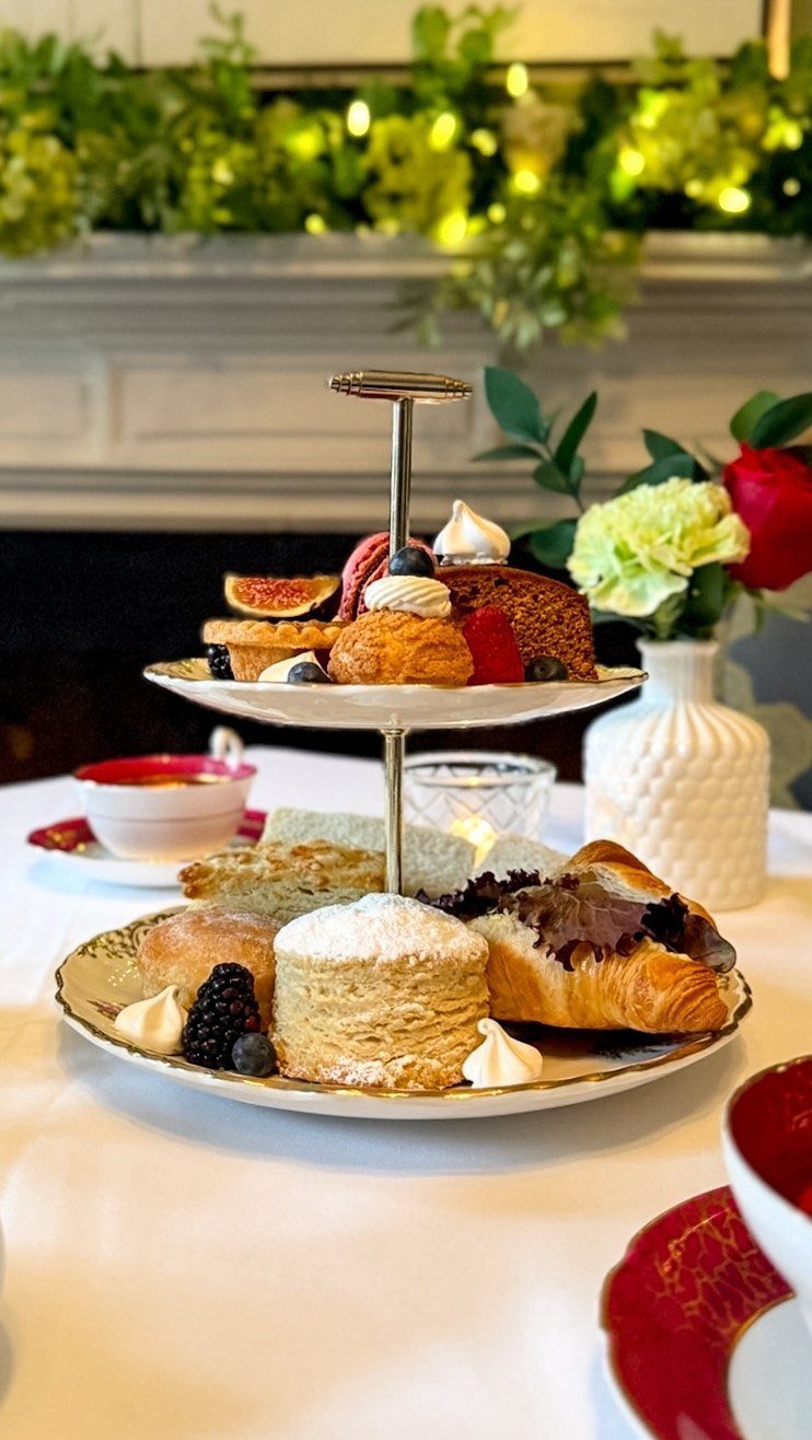 Two-tiered pastry stand with scones, croissants, and cake on a white tablecloth.