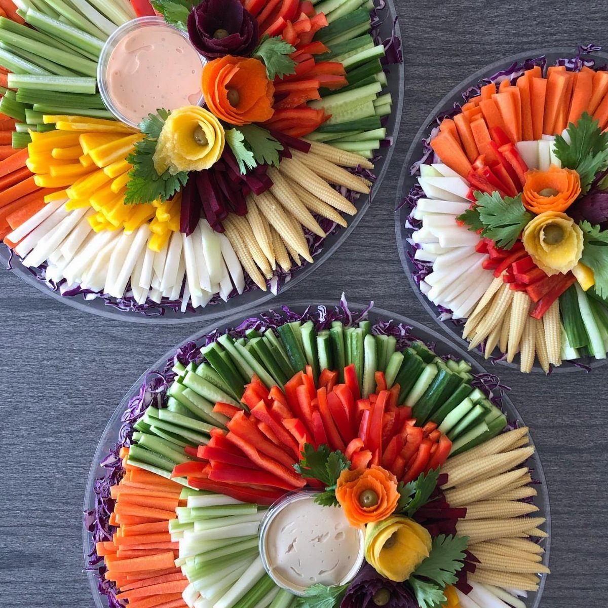 Three vegetable platters with hummus, featuring colorful sliced carrots, cucumbers, and baby corn.