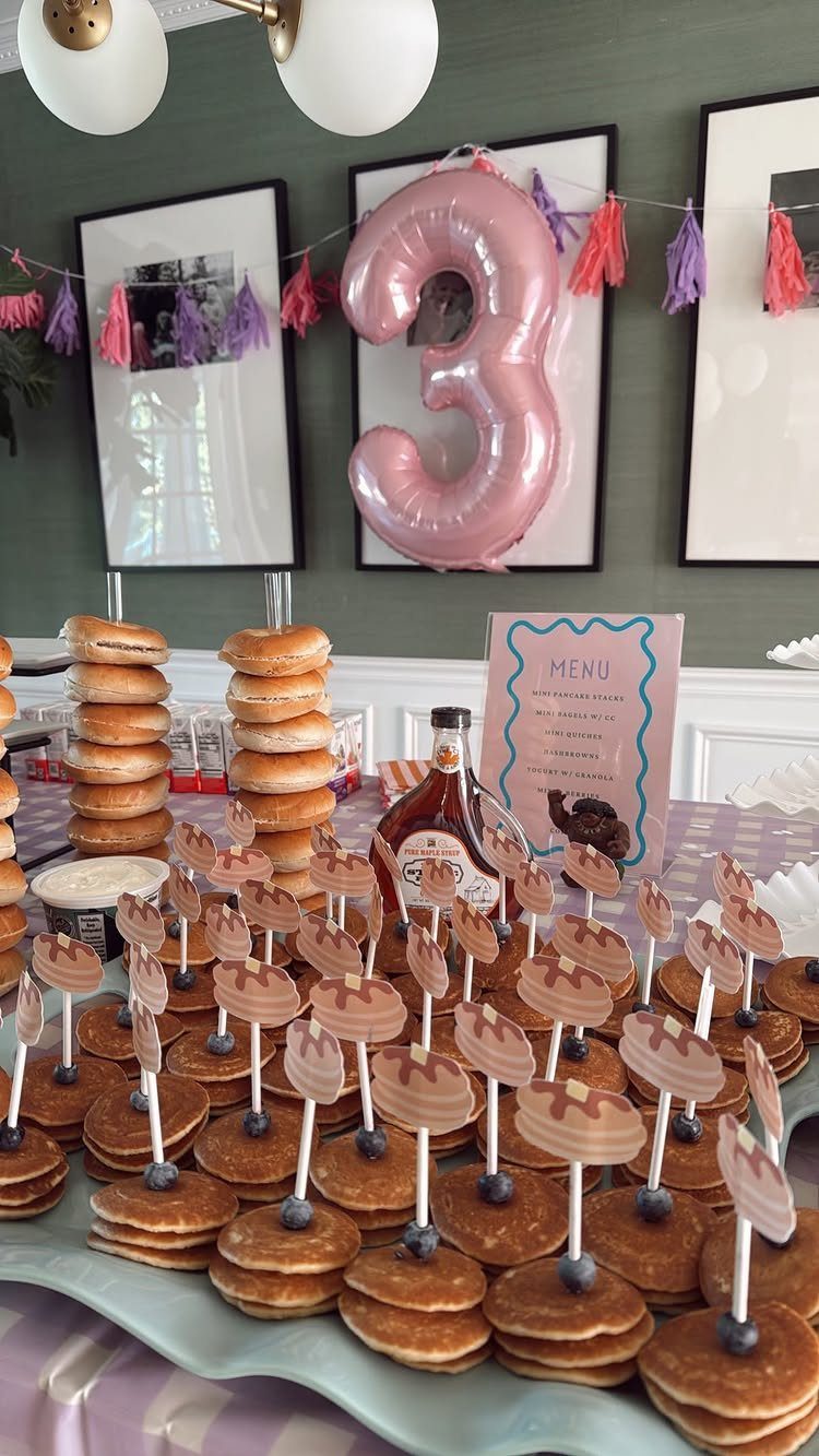 Mini pancake stacks with blueberry toppings and decorative toppers on a party table.