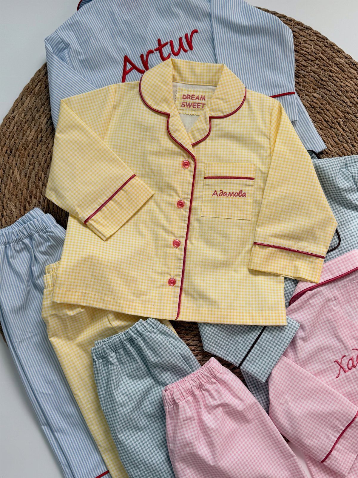 Children's gingham pajama sets in yellow, blue, and pink on a woven mat.