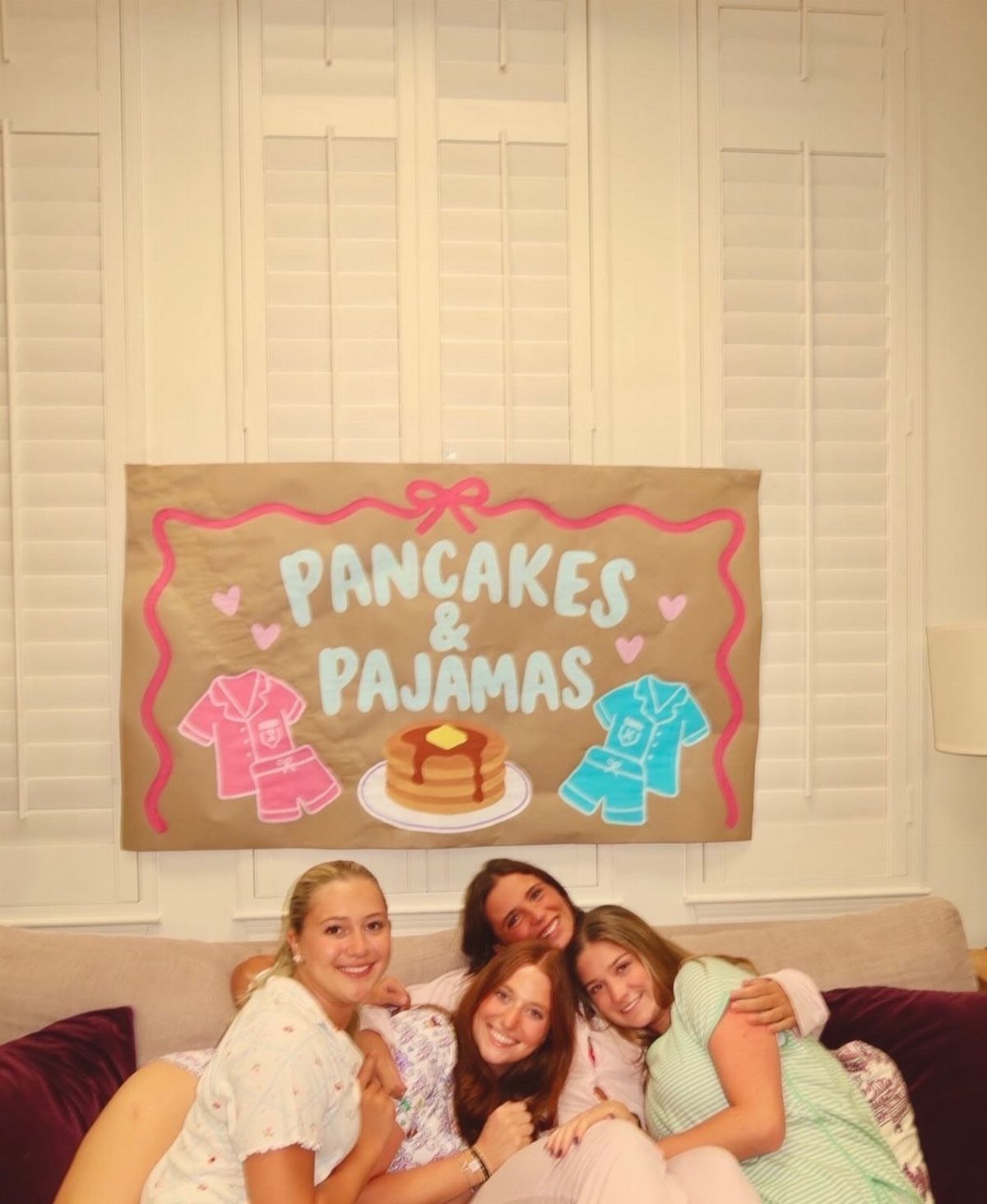 Four women in pajamas posing in front of a Pancakes and Pajamas banner.