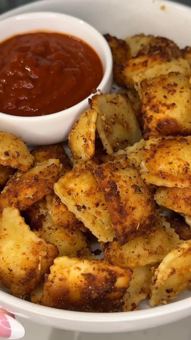 Crispy fried ravioli in a white bowl with a side of marinara sauce.