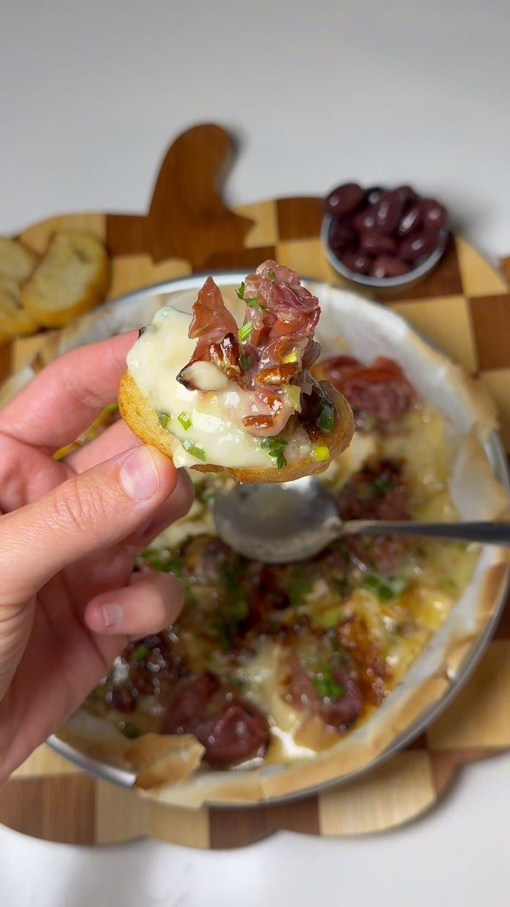 Toasted bread topped with melted brie and cured meat held over baking dish.